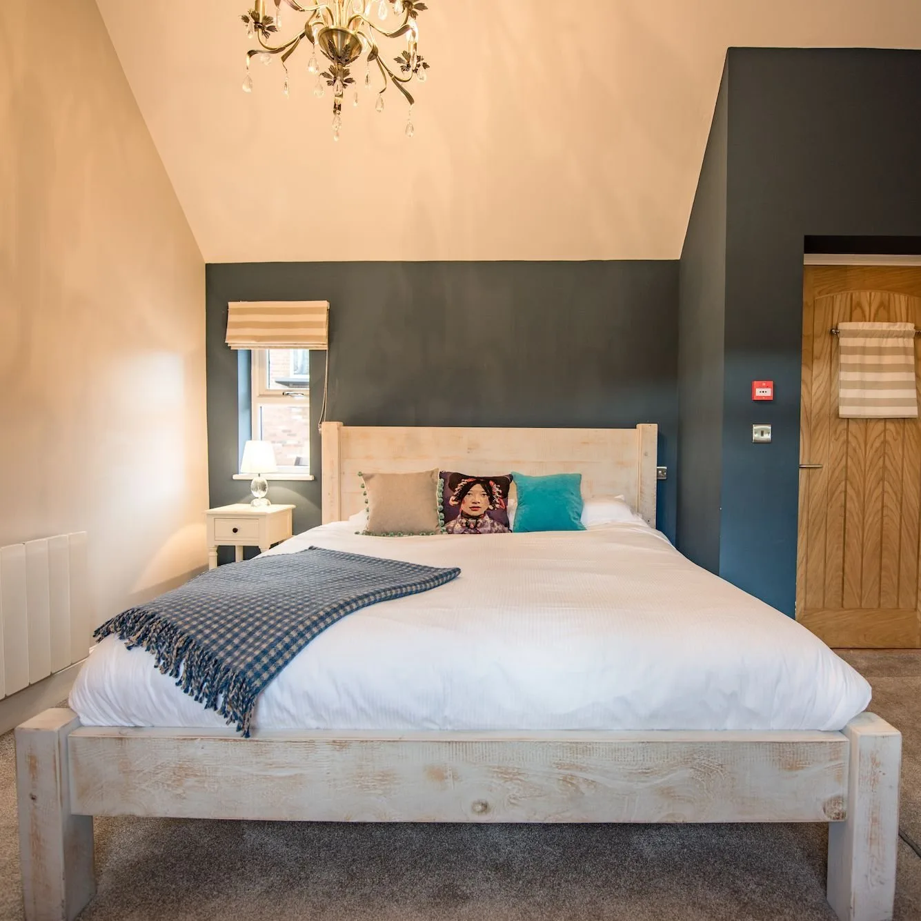 Bedroom with a charcoal feature wall, whitewashed timber bed and chandelier beneath a sloping ceiling.