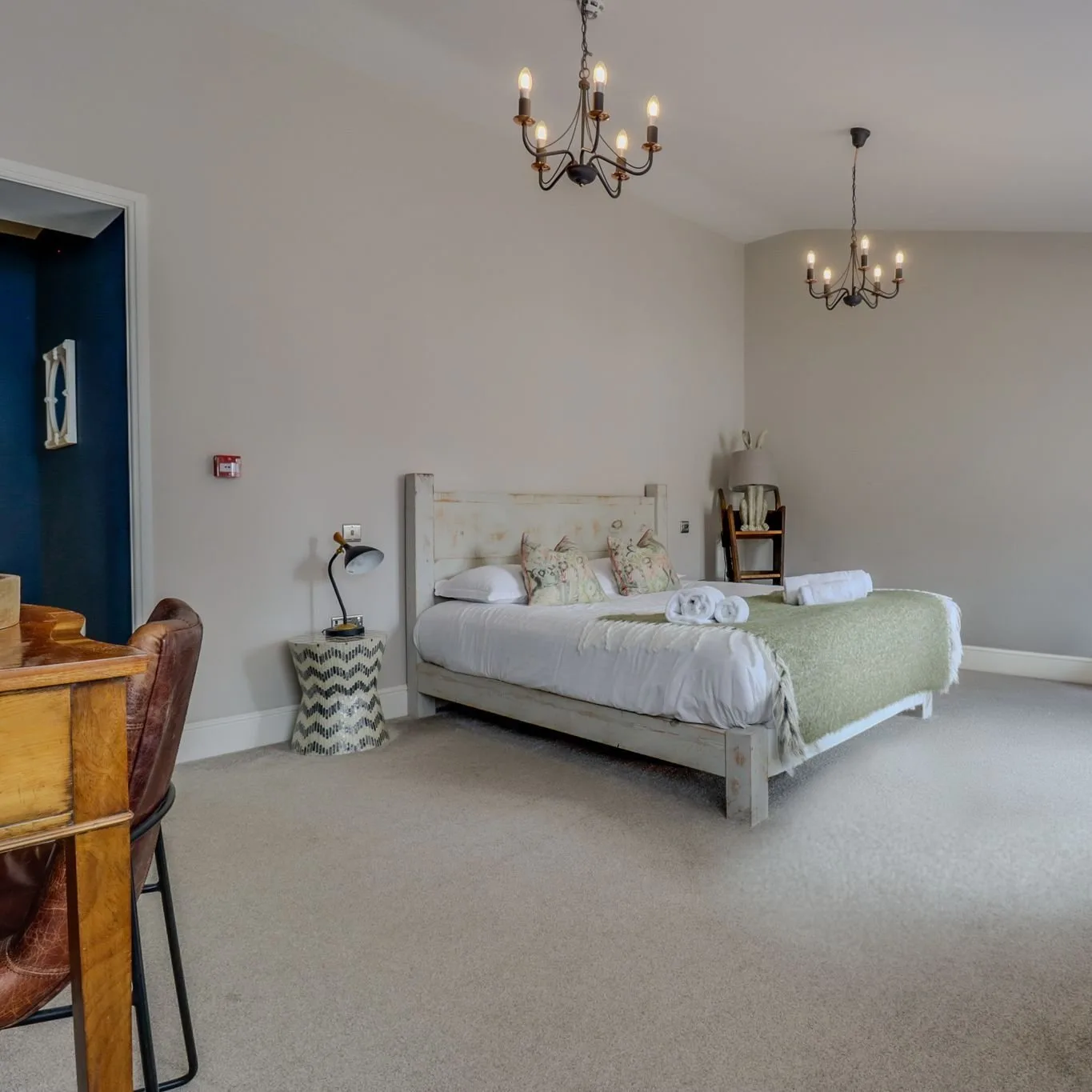 Large bedroom with two wrought-iron chandeliers, a wooden desk and a deep blue alcove.