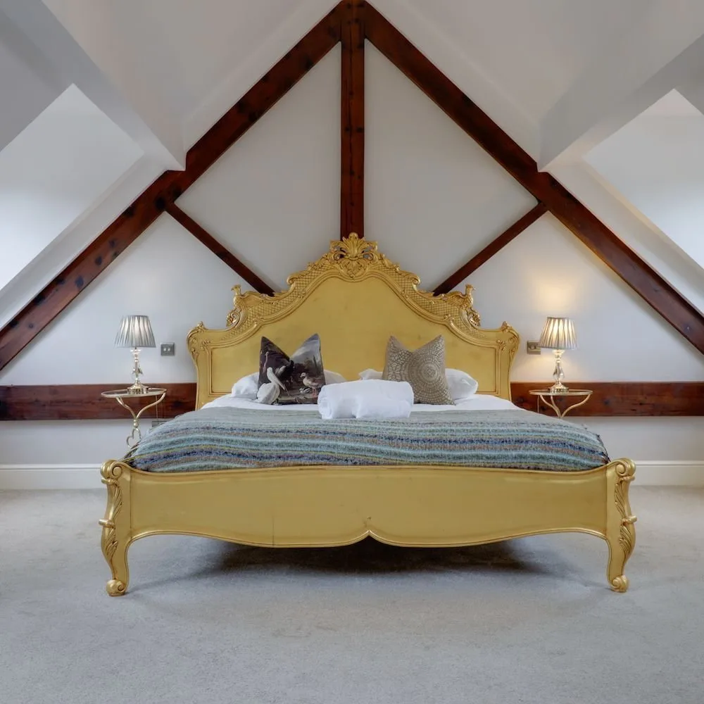 Bedroom beneath the eaves with exposed timber trusses and an ornate gilt bed frame.