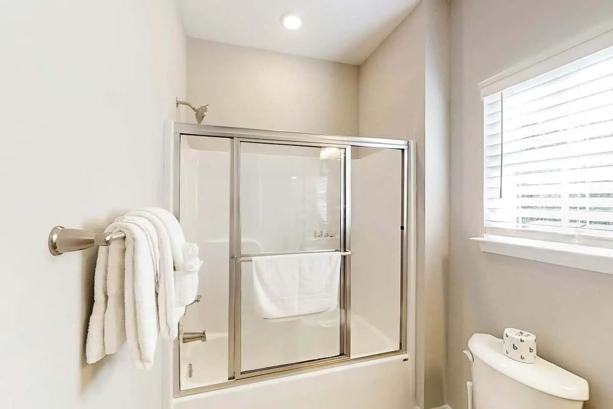 Un baño luminoso con una ducha de vidrio y una ventana con persianas.