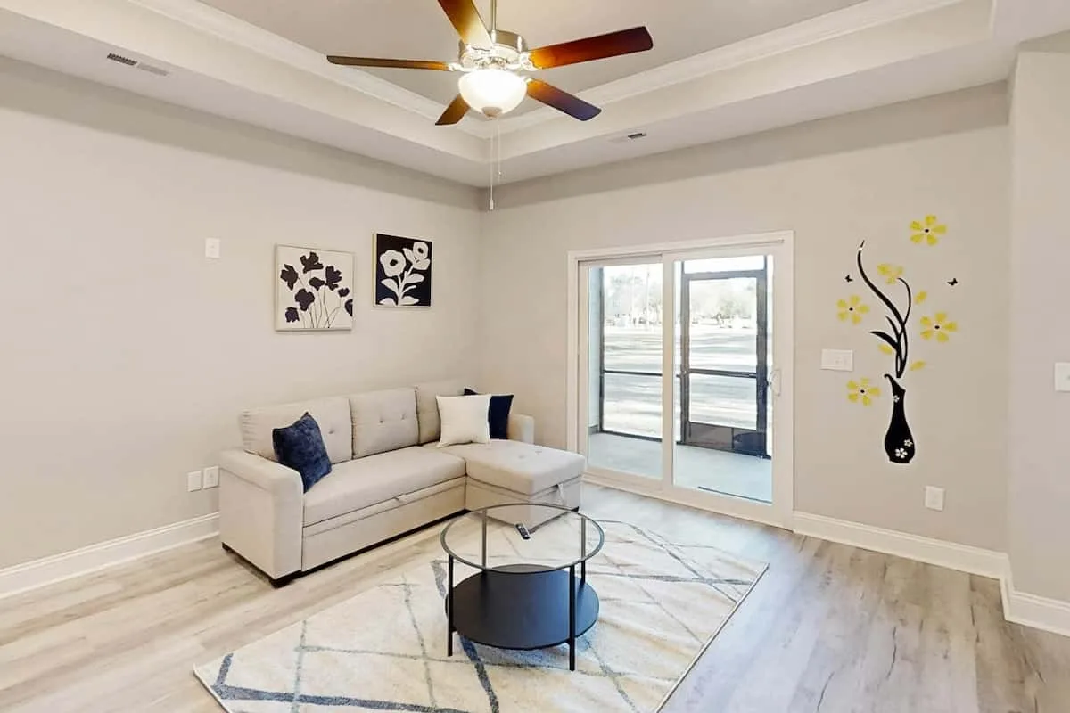 A bright living room with a sectional sofa and glass doors opening to a balcony.
