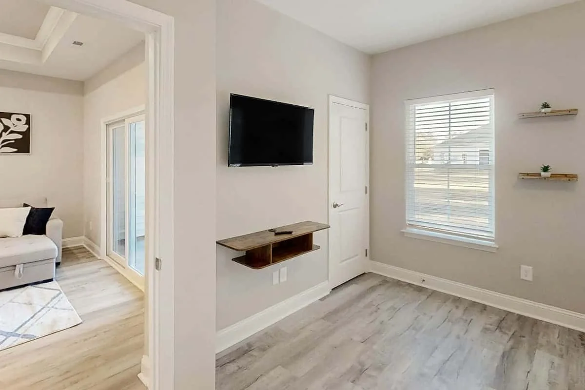 Una sala luminosa con un televisor montado en la pared y una ventana con persianas.