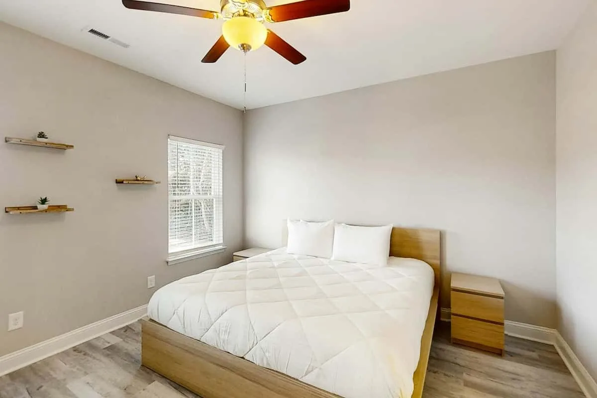 Un dormitorio luminoso con una cama bien arreglada y un ventilador de techo.
