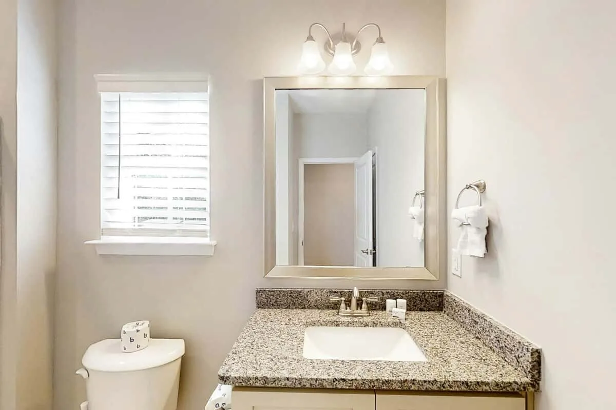 Un tocador de baño con lavabo y espejo está junto a una ventana.