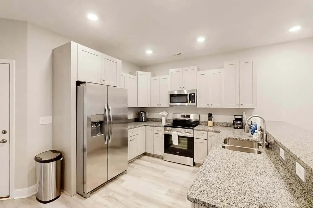 Una cocina luminosa con gabinetes blancos, electrodomésticos de acero inoxidable y una encimera larga.