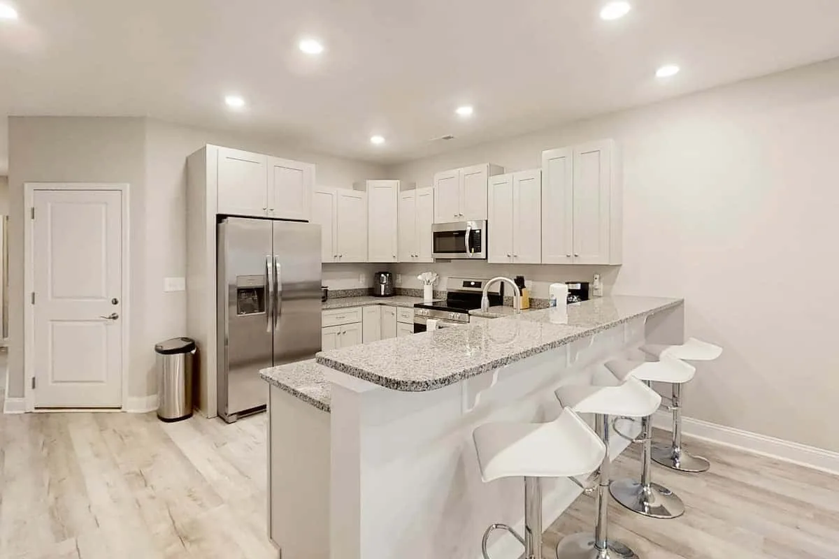 Una cocina luminosa con gabinetes blancos, un refrigerador de acero inoxidable y una isla para desayunar.