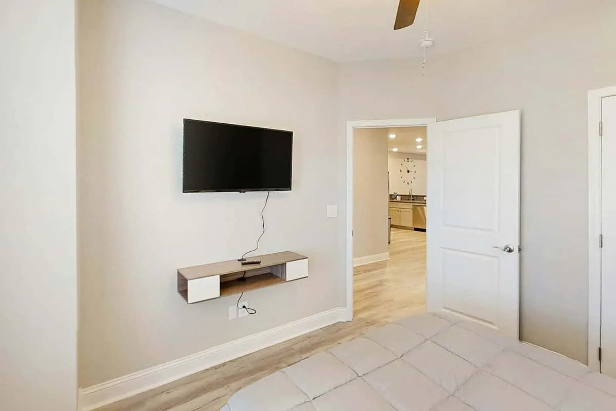 Un dormitorio con un televisor montado en la pared y una puerta abierta hacia la cocina.