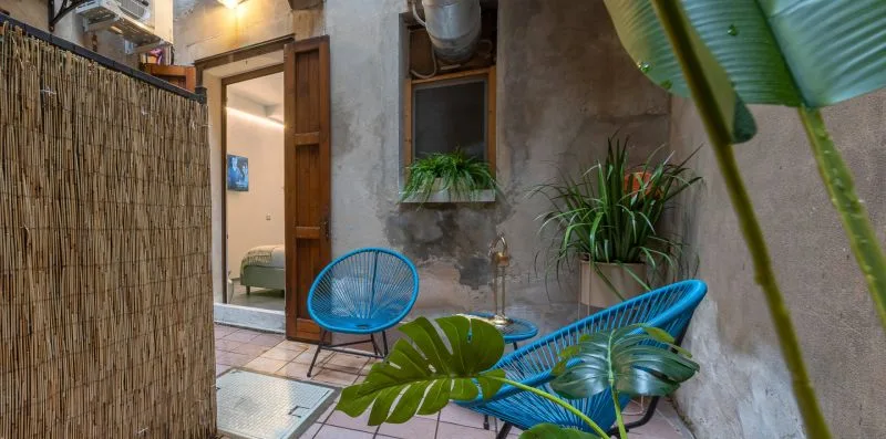 Un rincón de estar al aire libre con sillas azules, plantas y una pantalla de caña.