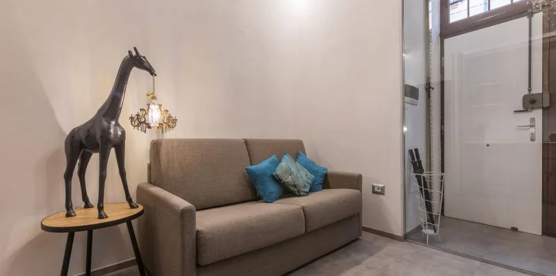 Una sala de estar con un sofá y una escultura de jirafa junto a la entrada.