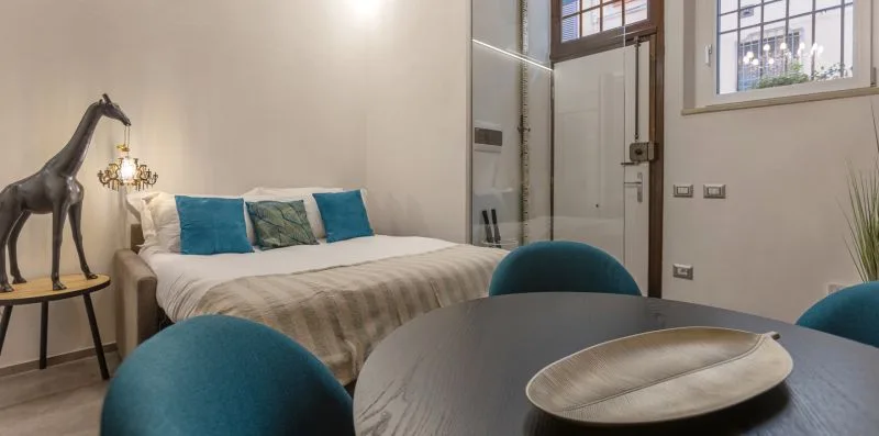 Dormitorio con una cama bien tendida, cojines azules y una mesa redonda.