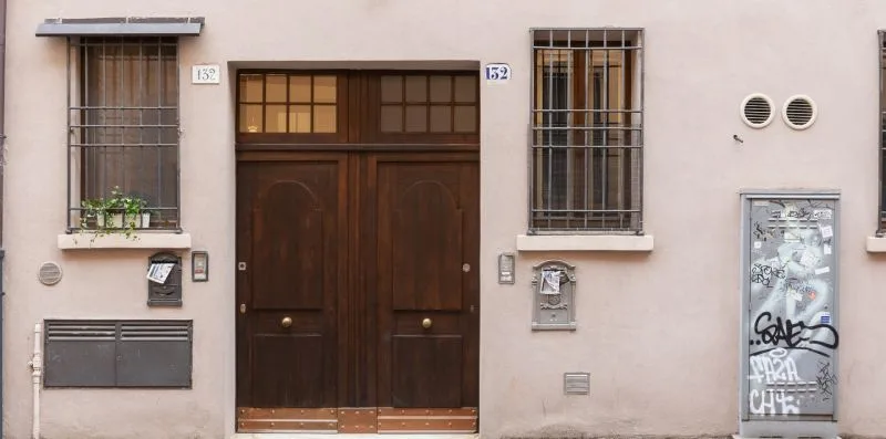 Una entrada de edificio con una puerta doble de madera oscura y ventanas con rejas.