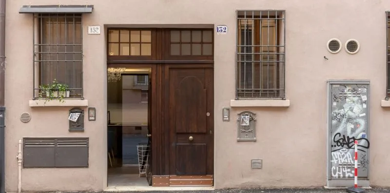 Entrada de un edificio con puerta de madera oscura, ventanas con rejas y un buzón en la pared.