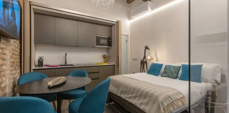 Un dormitorio con una cama, asientos azules y una pequeña zona de cocina.