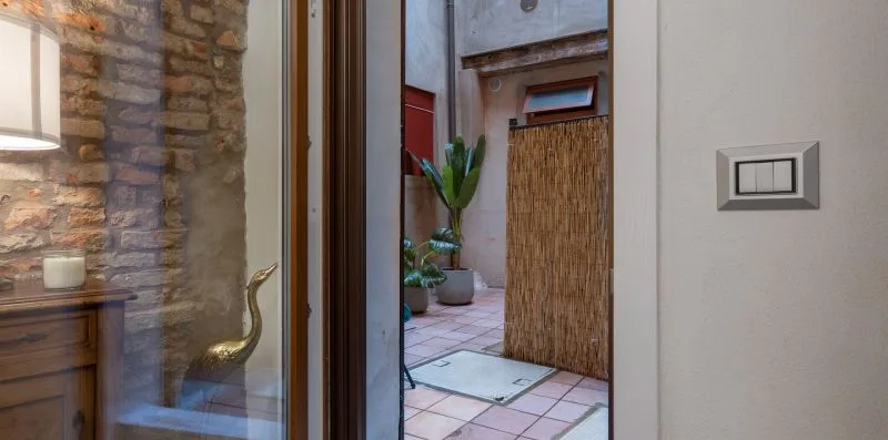Una puerta de vidrio da a un patio embaldosado con plantas en macetas y un panel tejido.