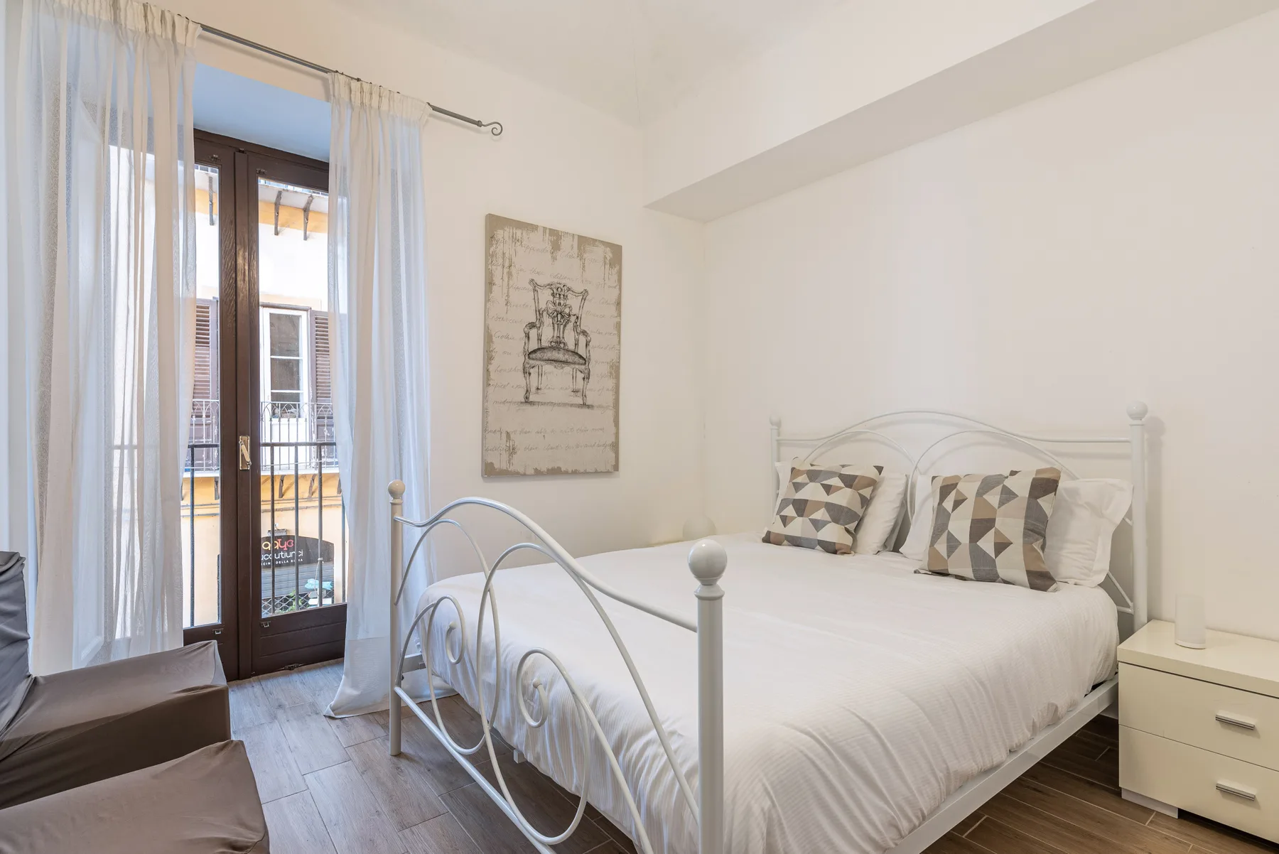 A bright bedroom with a white bed, patterned pillows, and a glass balcony door.