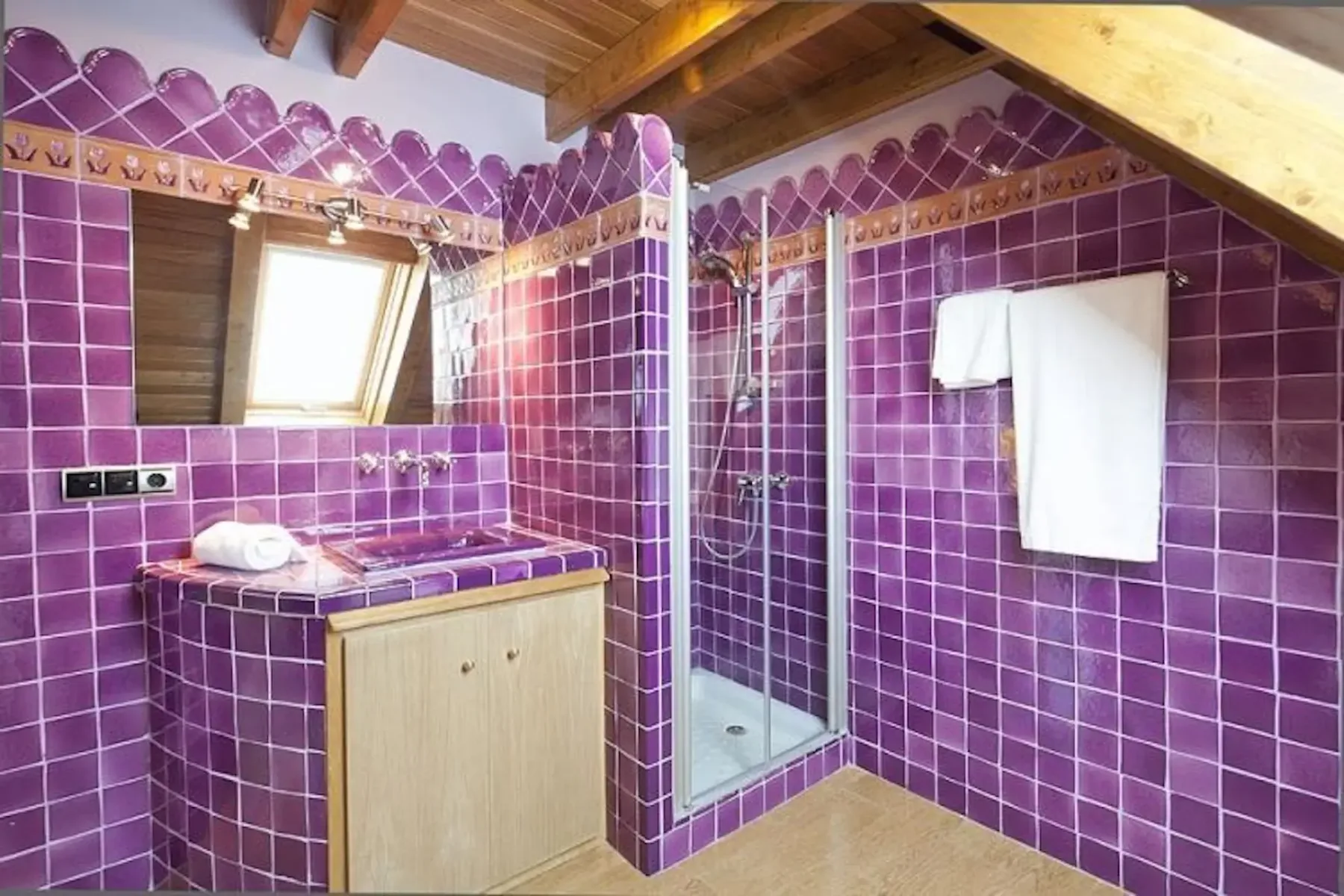 Bathroom with purple tiled walls, a wooden cabinet, a shower, a skylight, and towel hanging on a rack.