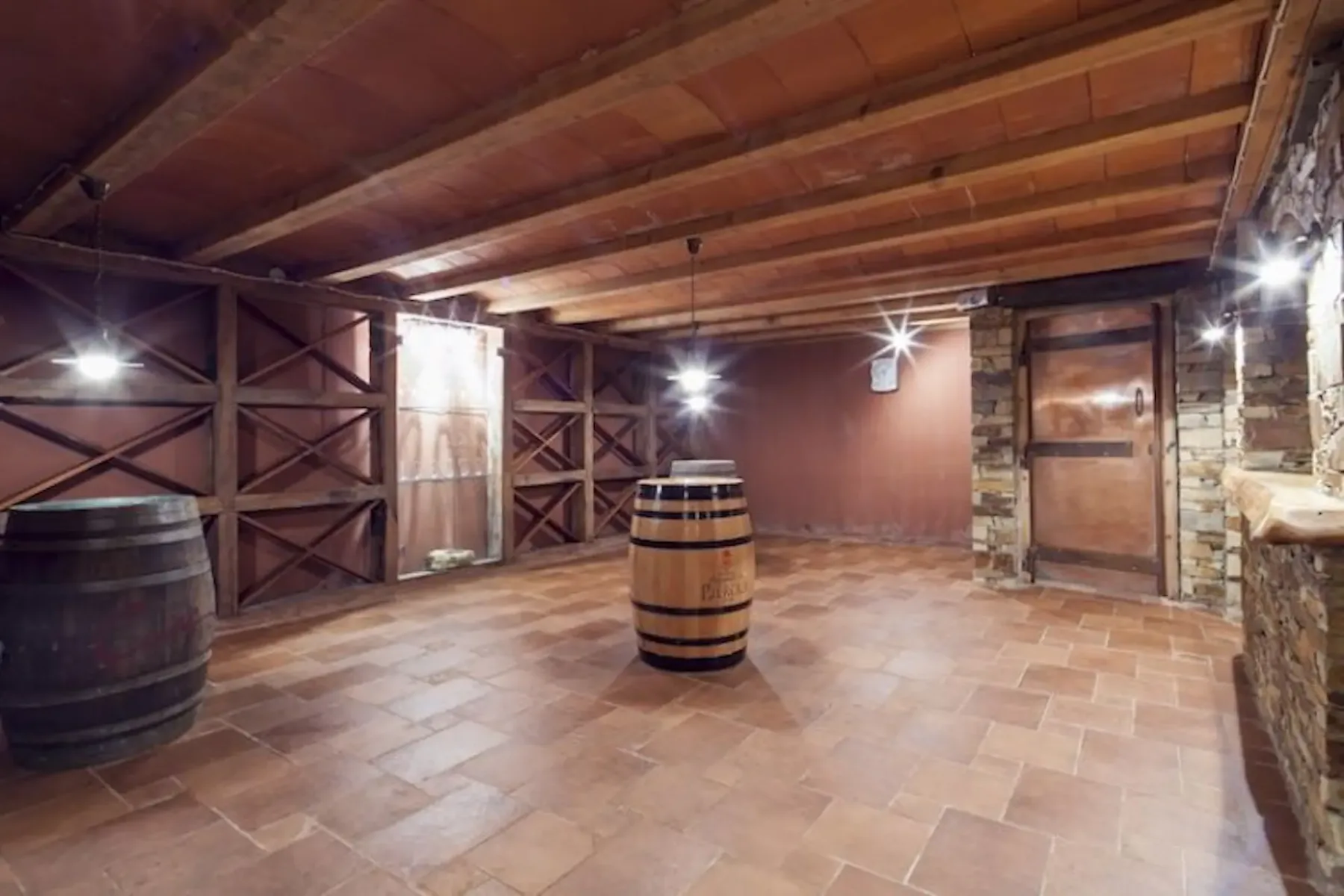 A rustic barrel room with exposed wooden beams and tiled flooring.