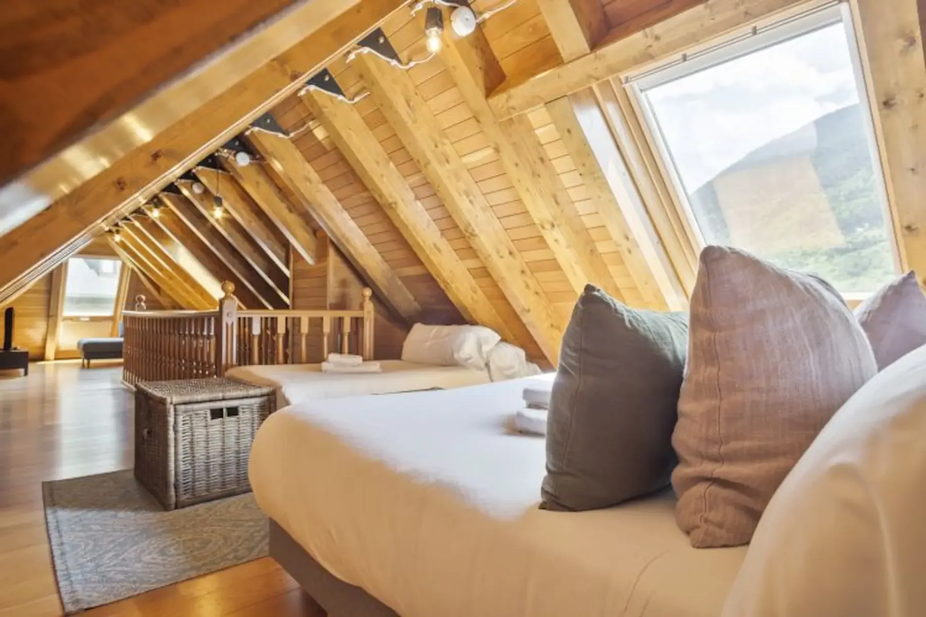 An attic bedroom with a bed, pillows, exposed wooden beams, and a large window.