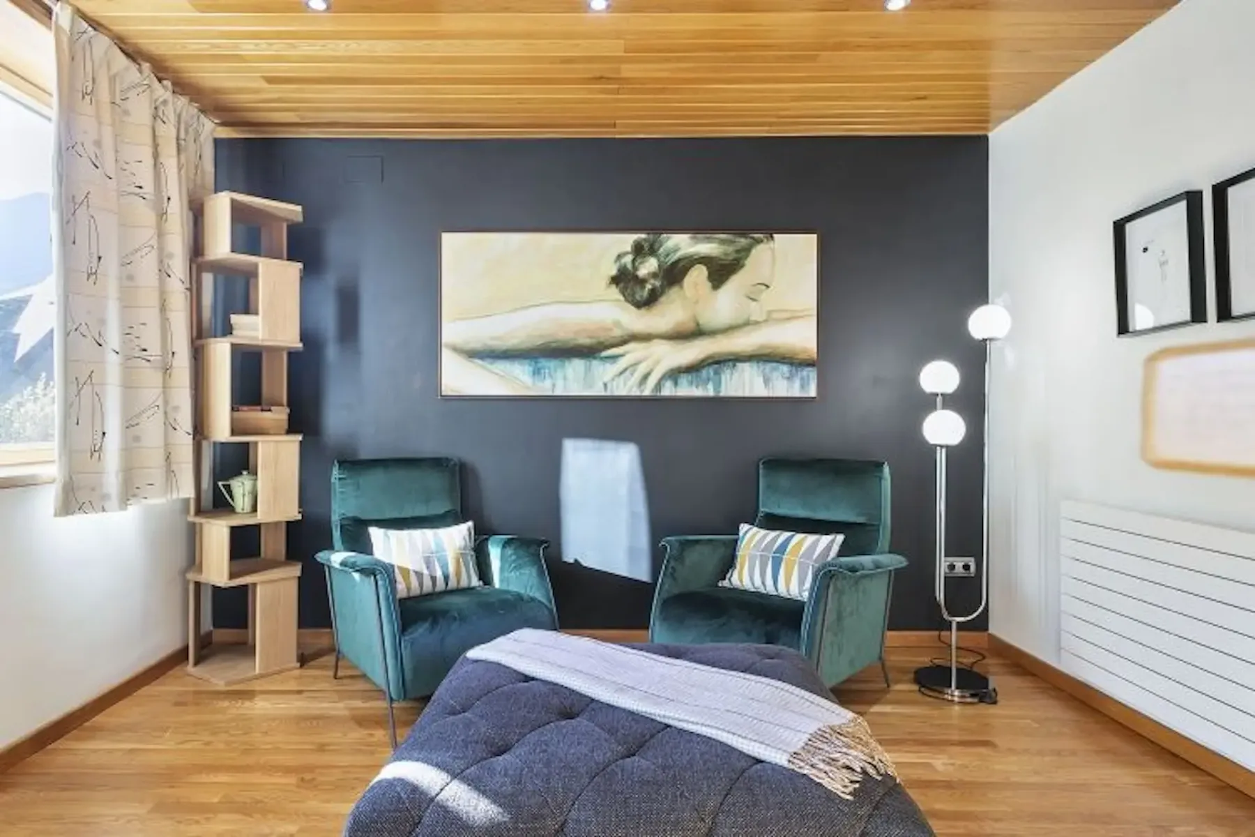A sitting room with green seating, a framed painting, and a floor lamp.