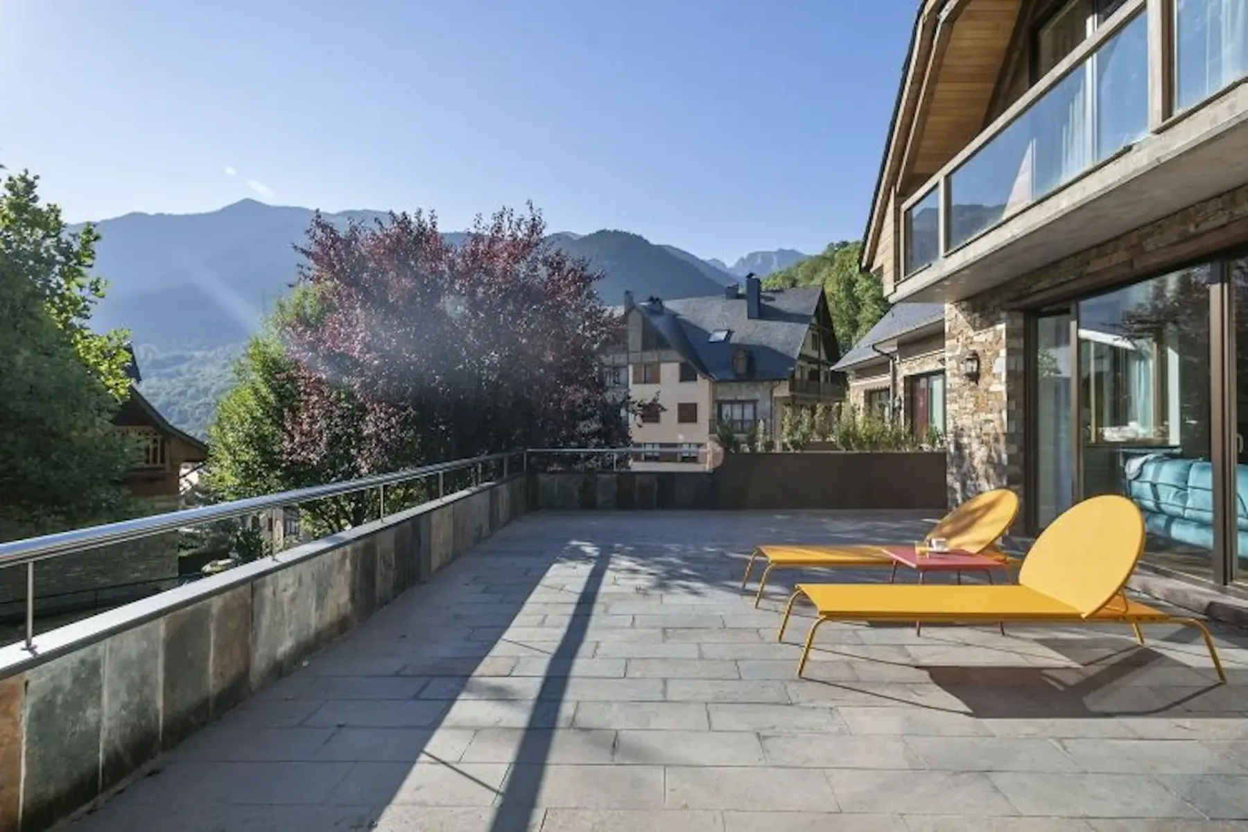 A spacious stone terrace with yellow lounge chairs and mountain views.