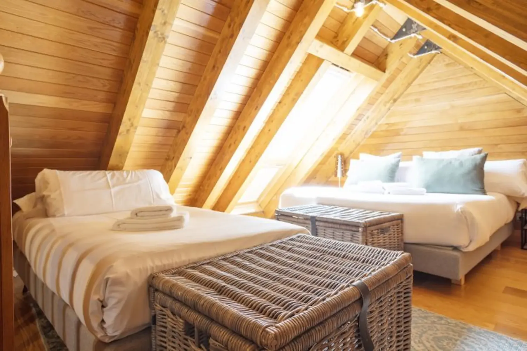 A wood-paneled attic bedroom with two beds and woven storage baskets.