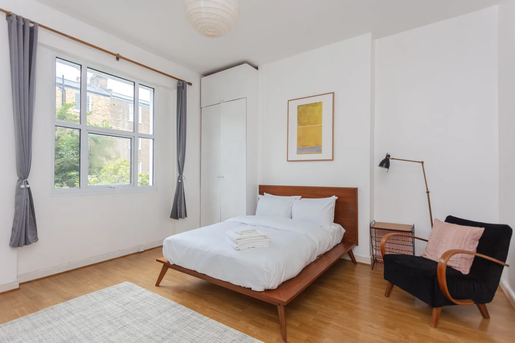 A bright bedroom with a neatly made bed and a large curtained window.