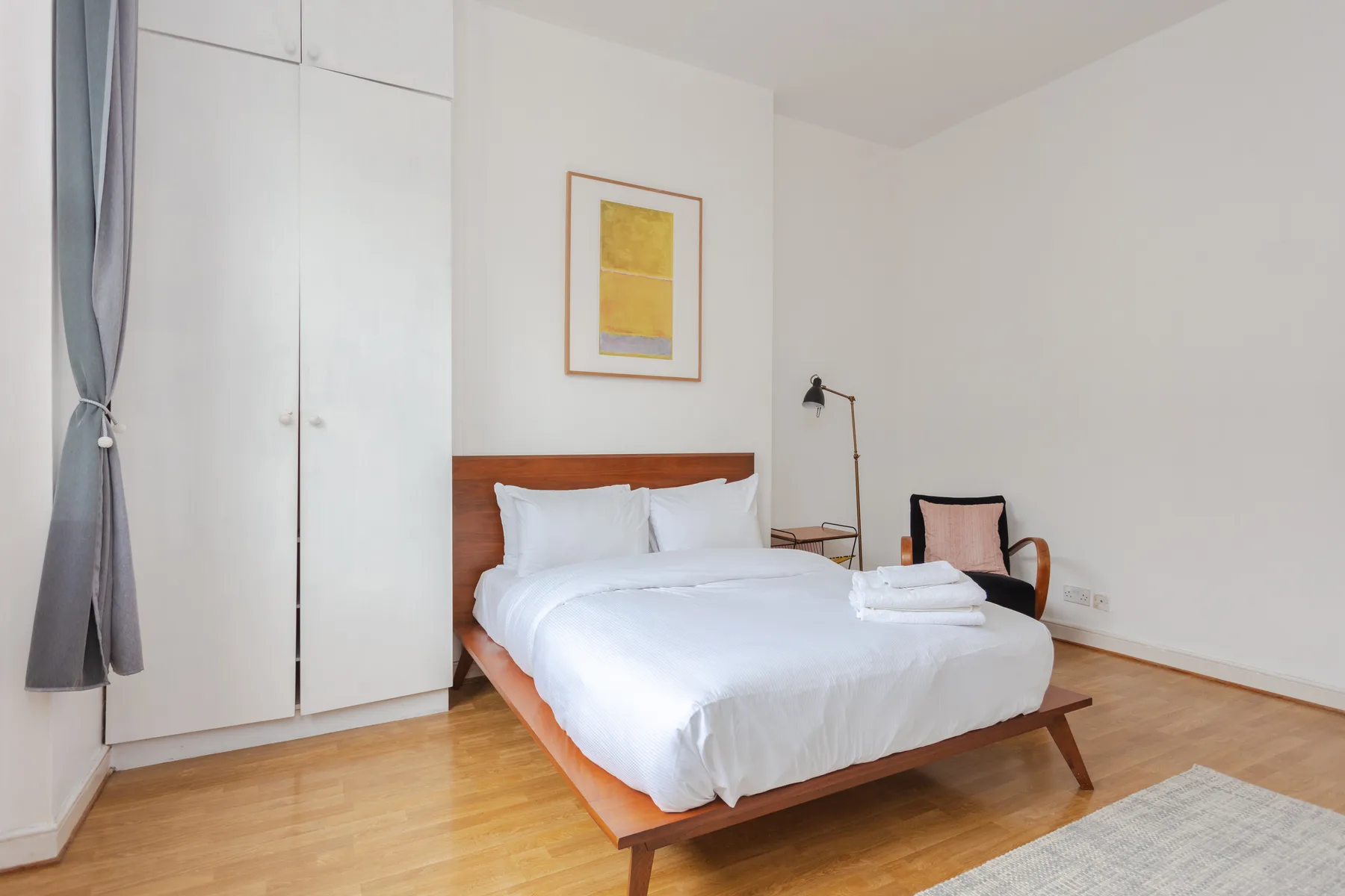 Un dormitorio luminoso con una cama, un armario y un cuadro en la pared.