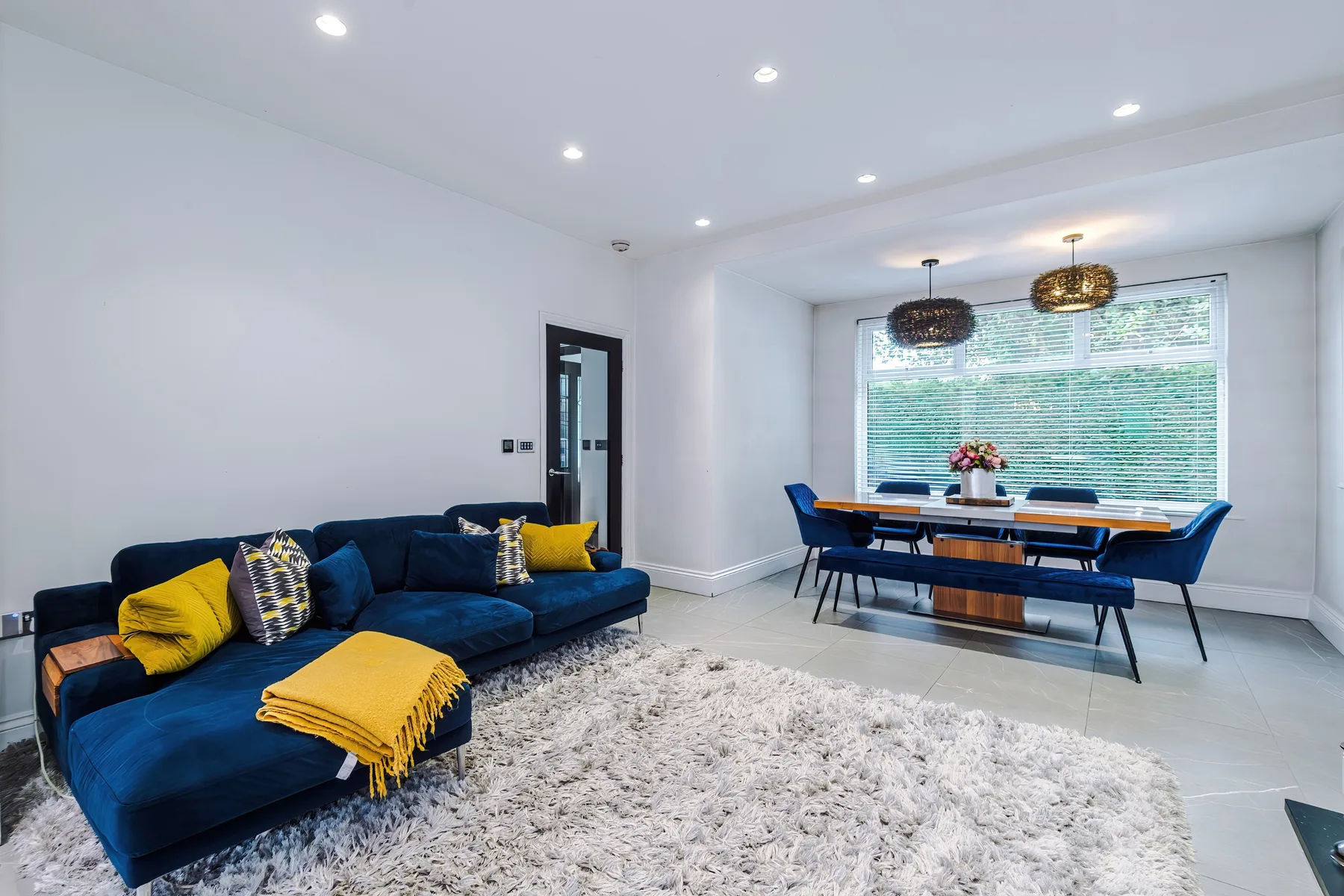 A bright living and dining room with blue seating beside a dining table.