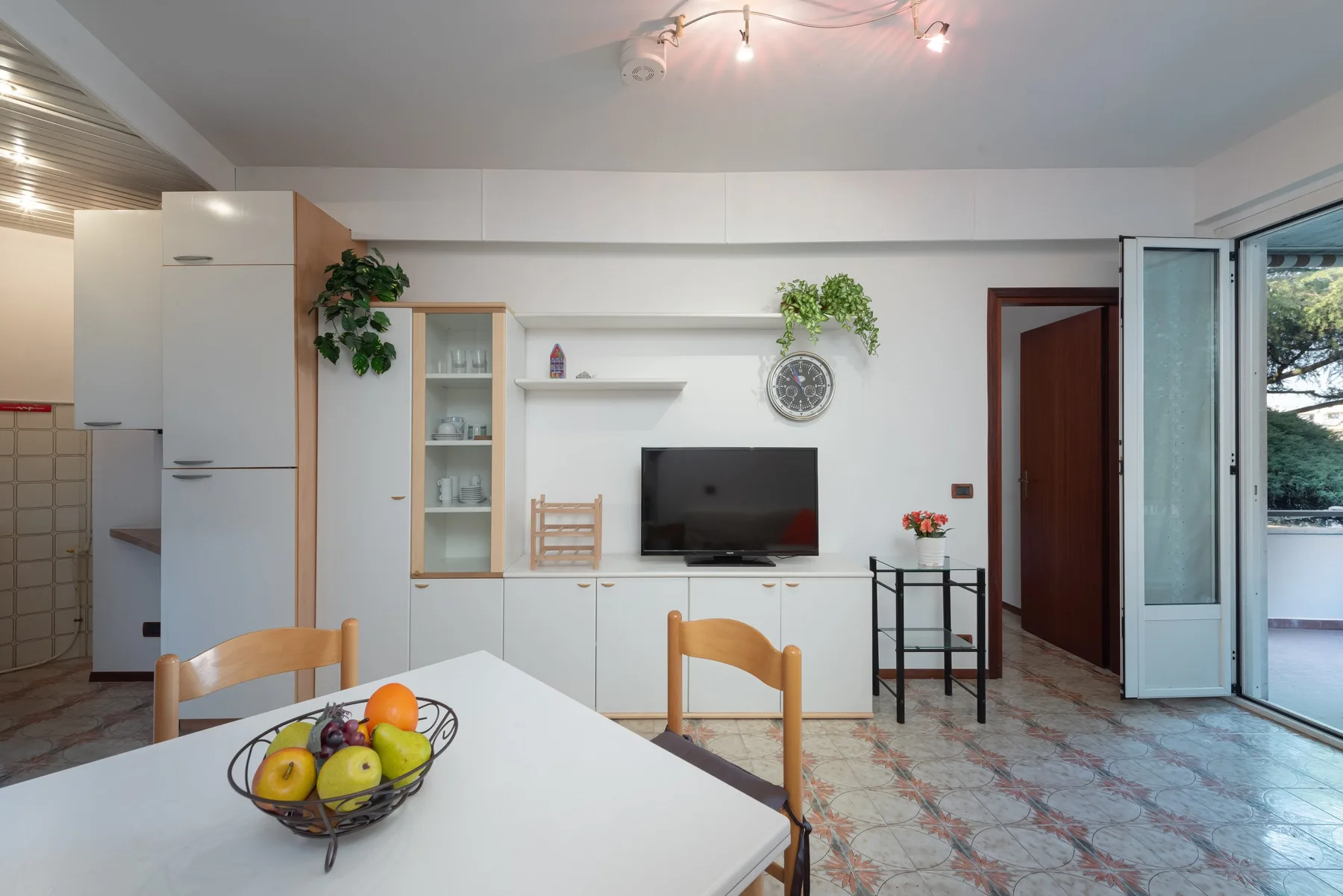 Un luminoso comedor y sala de estar con una mesa, un televisor y puertas abiertas al balcón.