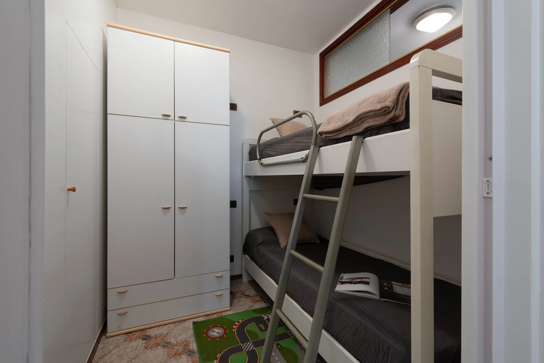 Un dormitorio compacto con literas, un armario y una pequeña alfombra de juegos.