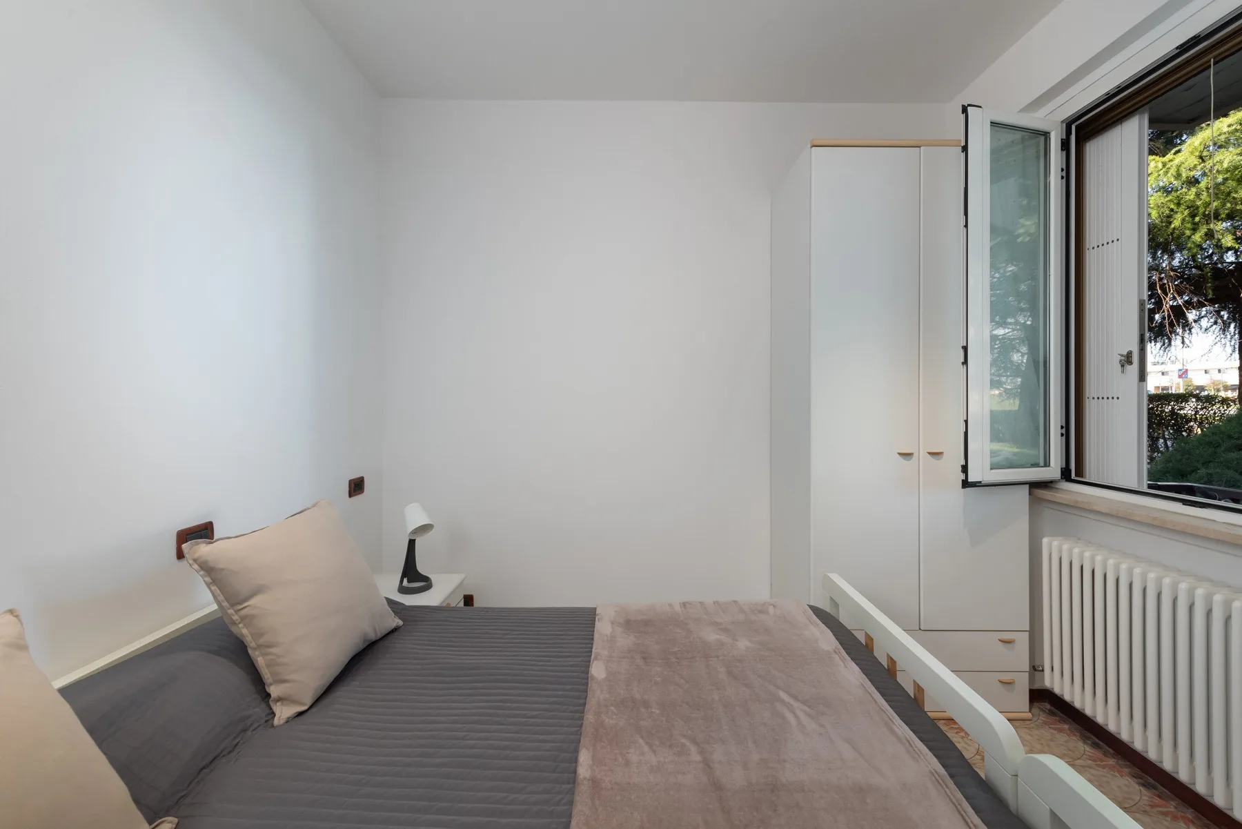 Un dormitorio con una cama junto a una ventana abierta y un radiador.
