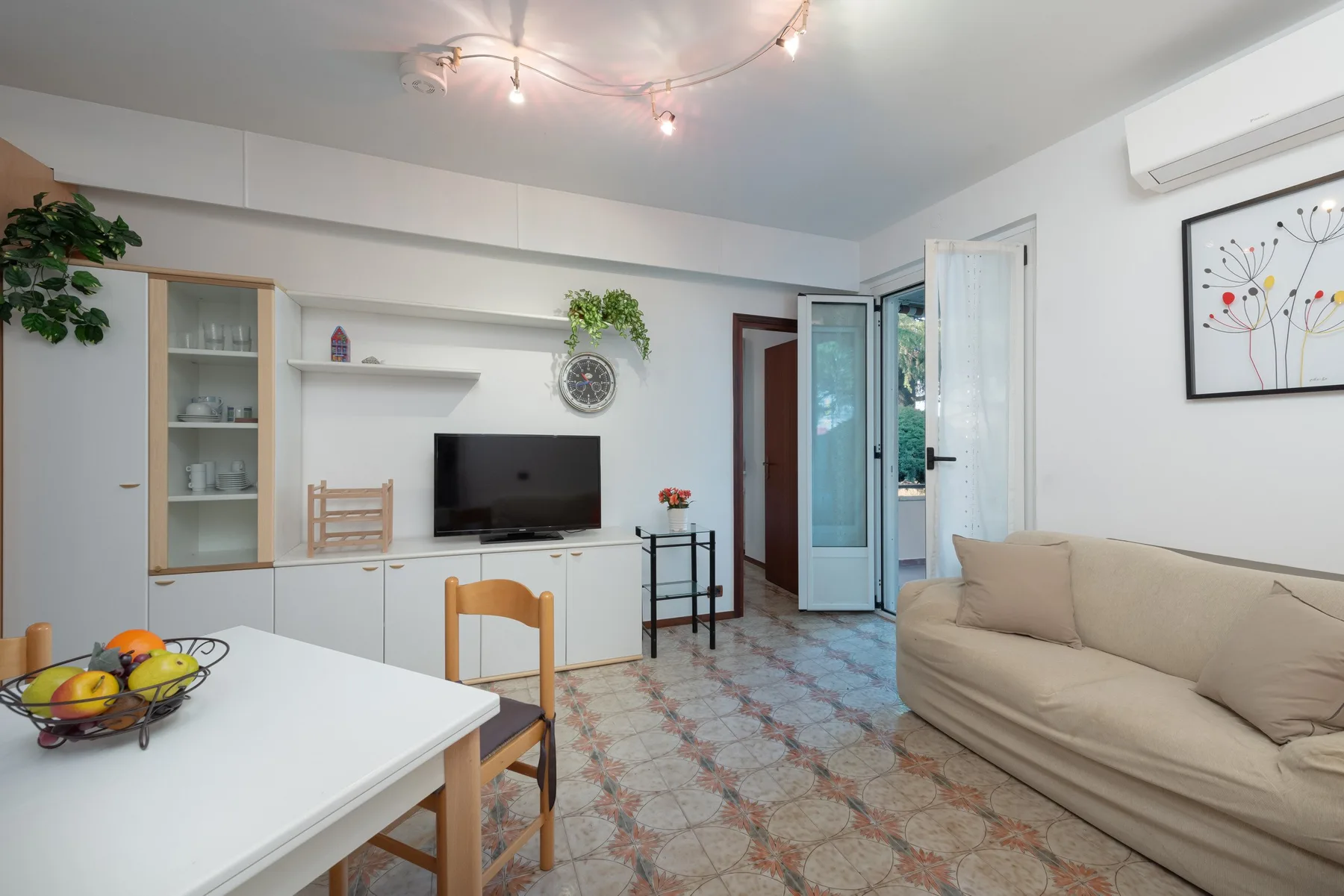 Una sala luminosa con asientos, un televisor y una puerta de vidrio abierta.