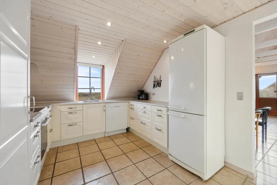 Una cocina luminosa con armarios blancos, un refrigerador y una ventana.
