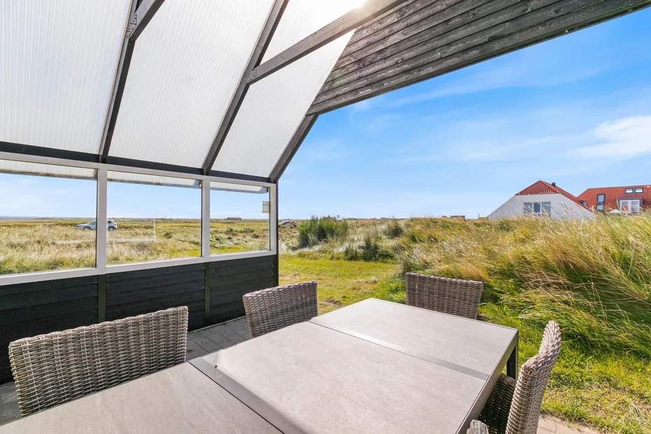 Una zona de comedor exterior cubierta, con mesa y asientos tejidos, da a dunas cubiertas de hierba.