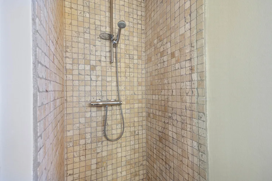 Una ducha alicatada con alcachofa de mano y controles montados en la pared.