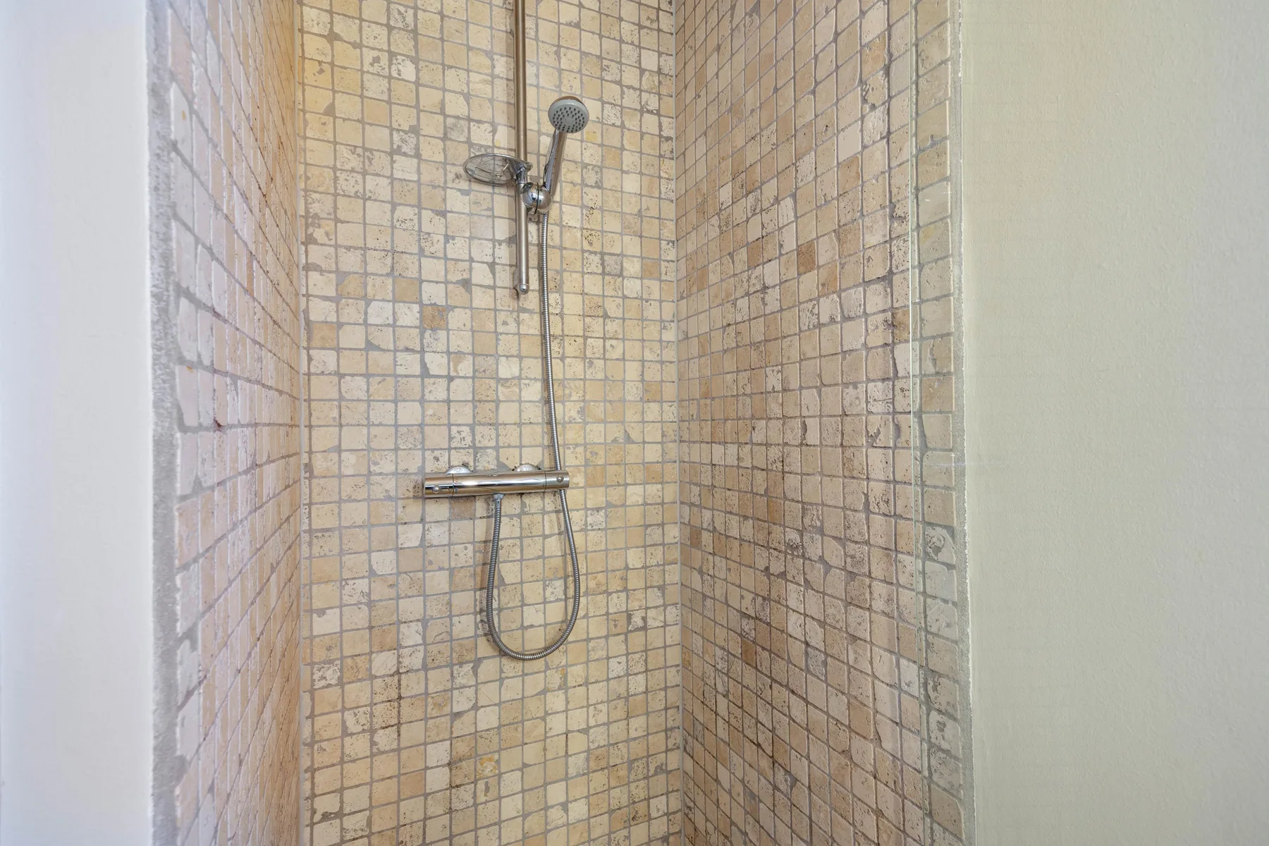 Una ducha con azulejos, ducha de mano y accesorios metálicos.