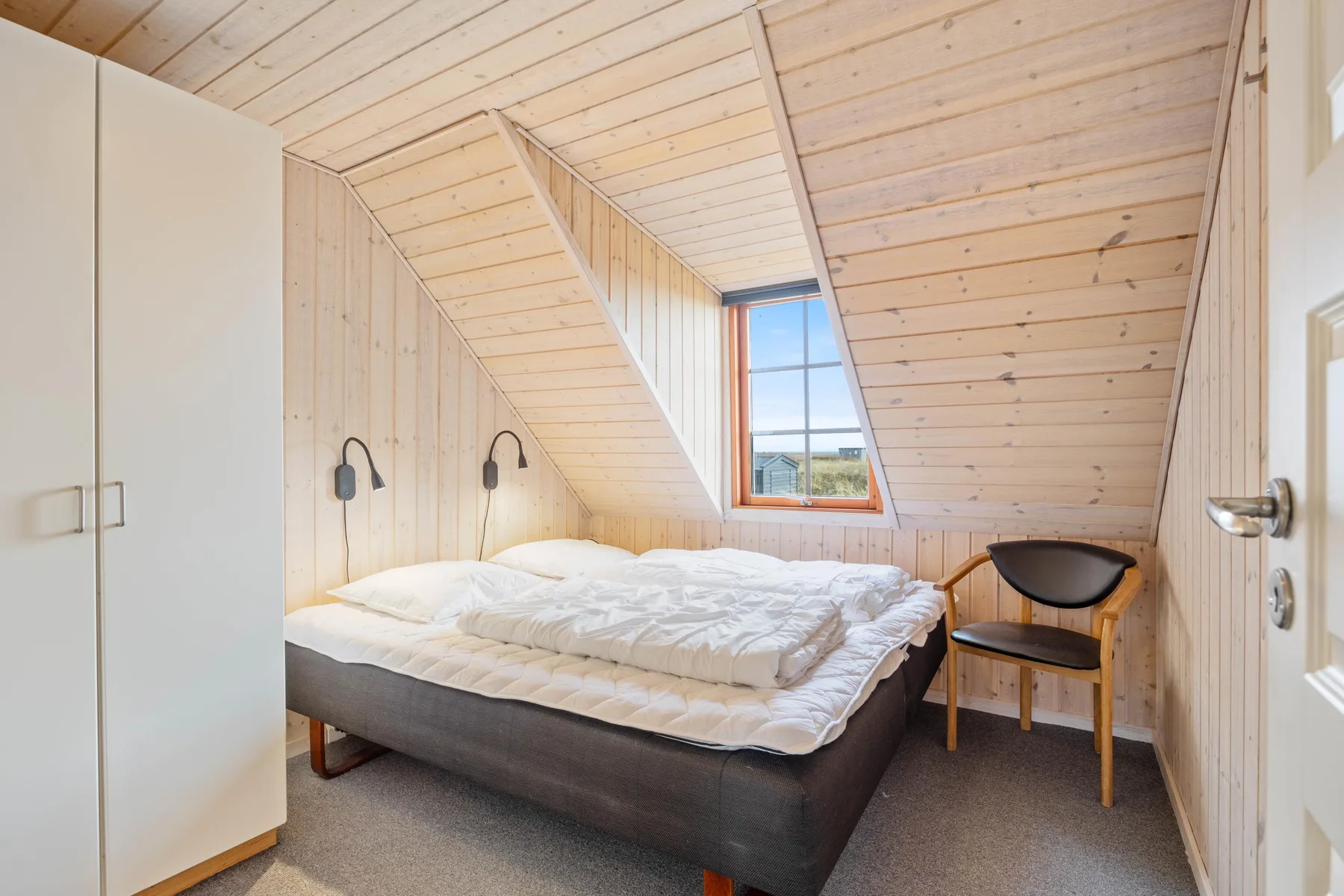 Un dormitorio con una cama bajo un techo de madera inclinado.