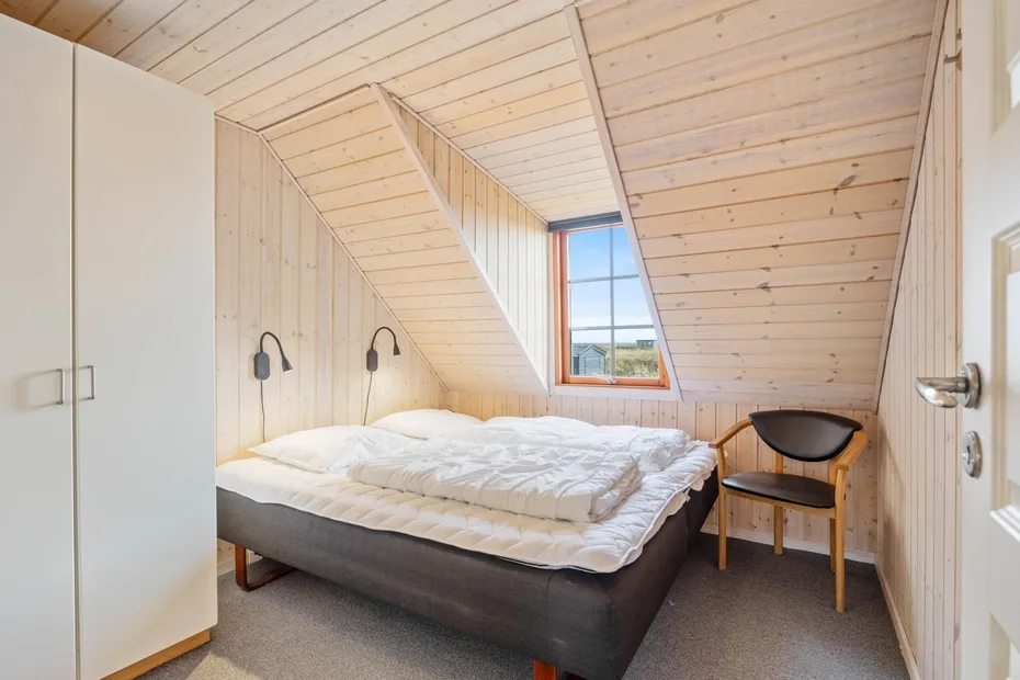 Un dormitorio con una cama, una ventana y una silla de madera.