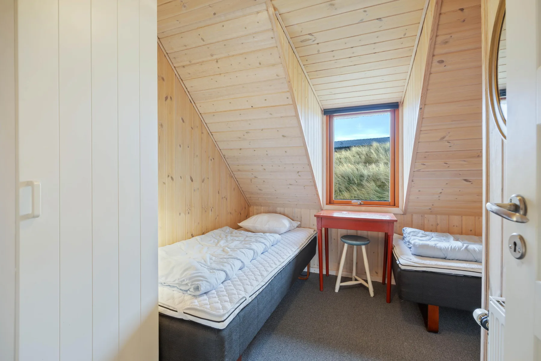Un dormitorio compacto con dos camas individuales y una mesita bajo la ventana.