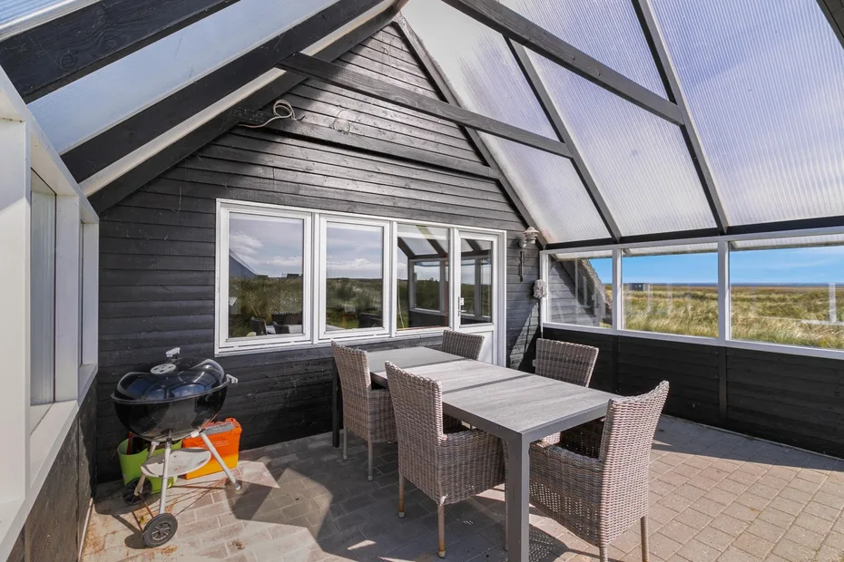 Una zona de comedor exterior cubierta con una mesa y asientos junto a amplias ventanas.