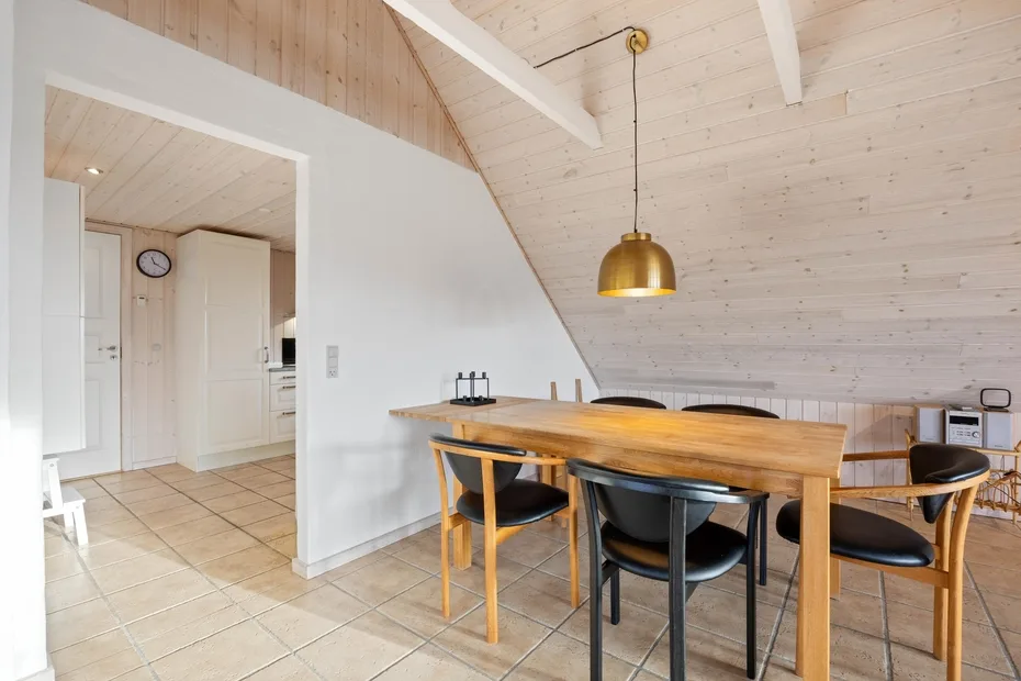 Comedor con una mesa de madera y sillas bajo un techo inclinado.