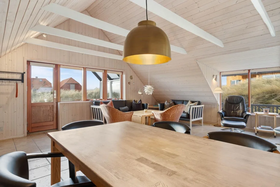 Una luminosa zona de comedor y estar tiene una gran mesa de madera y ventanas.