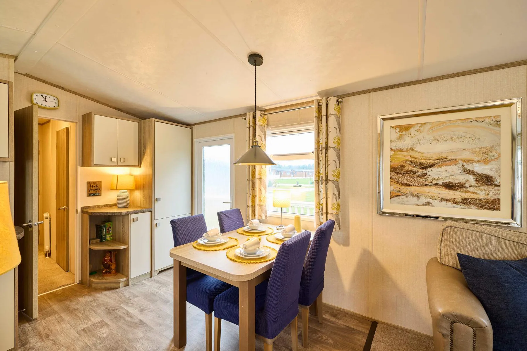 Comedor con la mesa puesta junto a una ventana y una obra enmarcada.