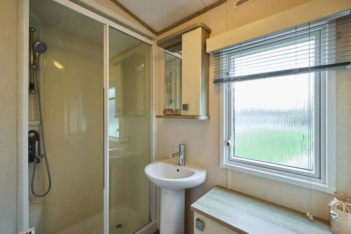 Un baño con ducha de cristal, lavabo con pedestal y ventana.