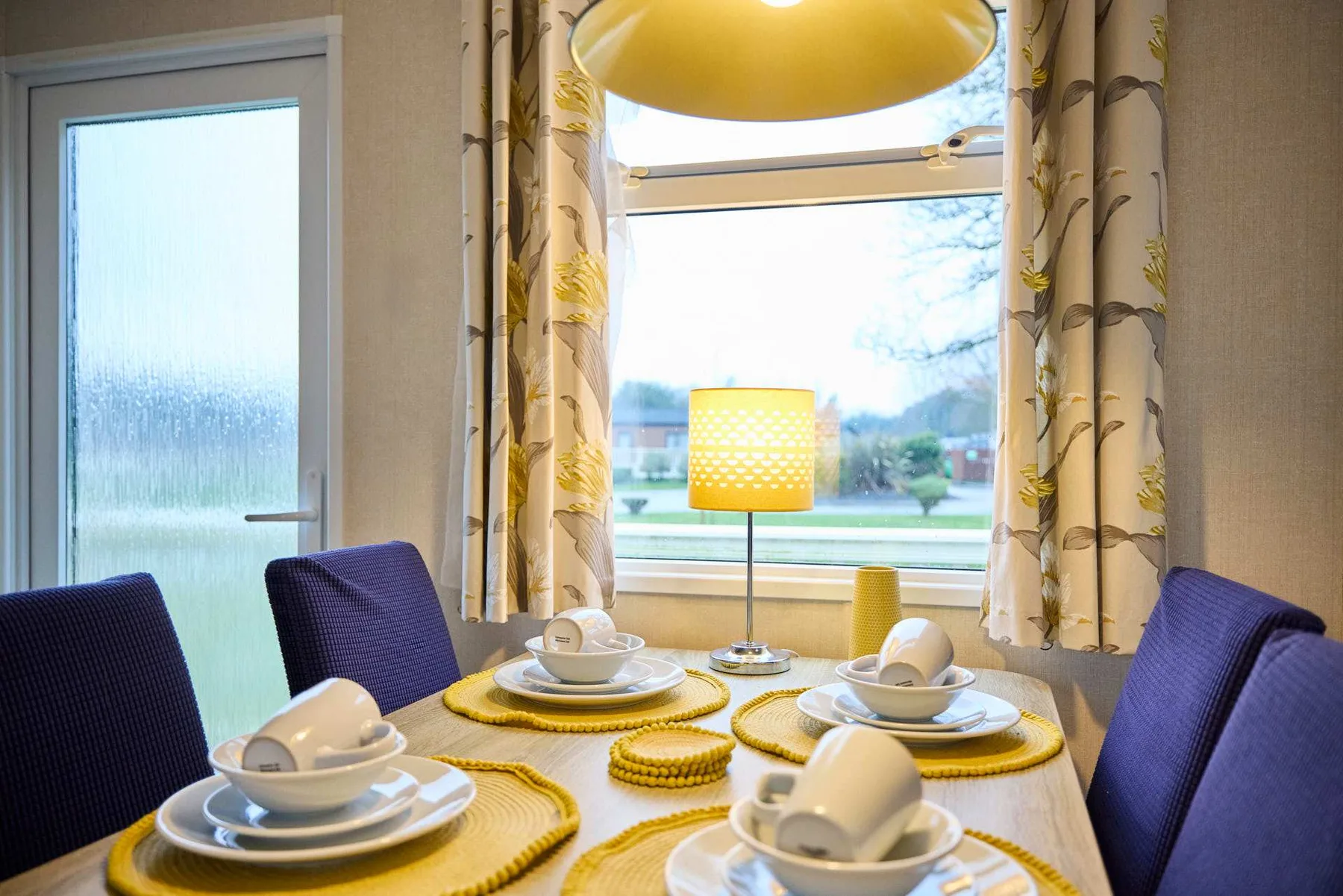 Comedor con una mesa puesta con platos junto a una ventana grande.