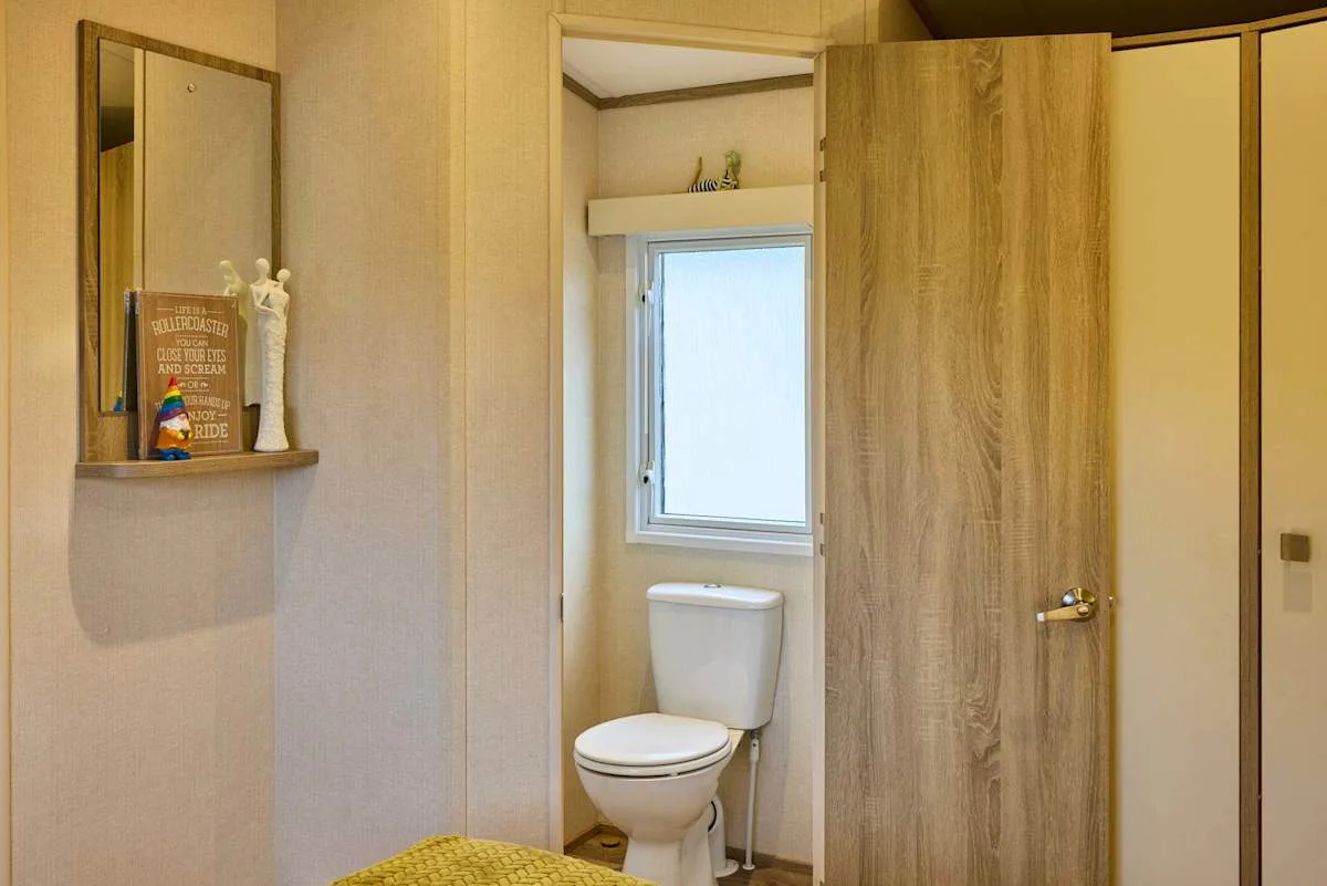 Baño con un inodoro bajo una ventana y una puerta de madera abierta.