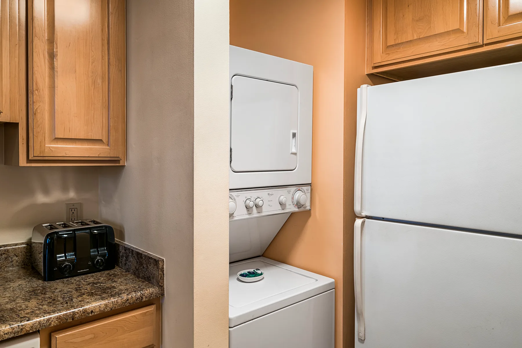 Área de lavandería con lavadora y secadora apiladas junto a un refrigerador.