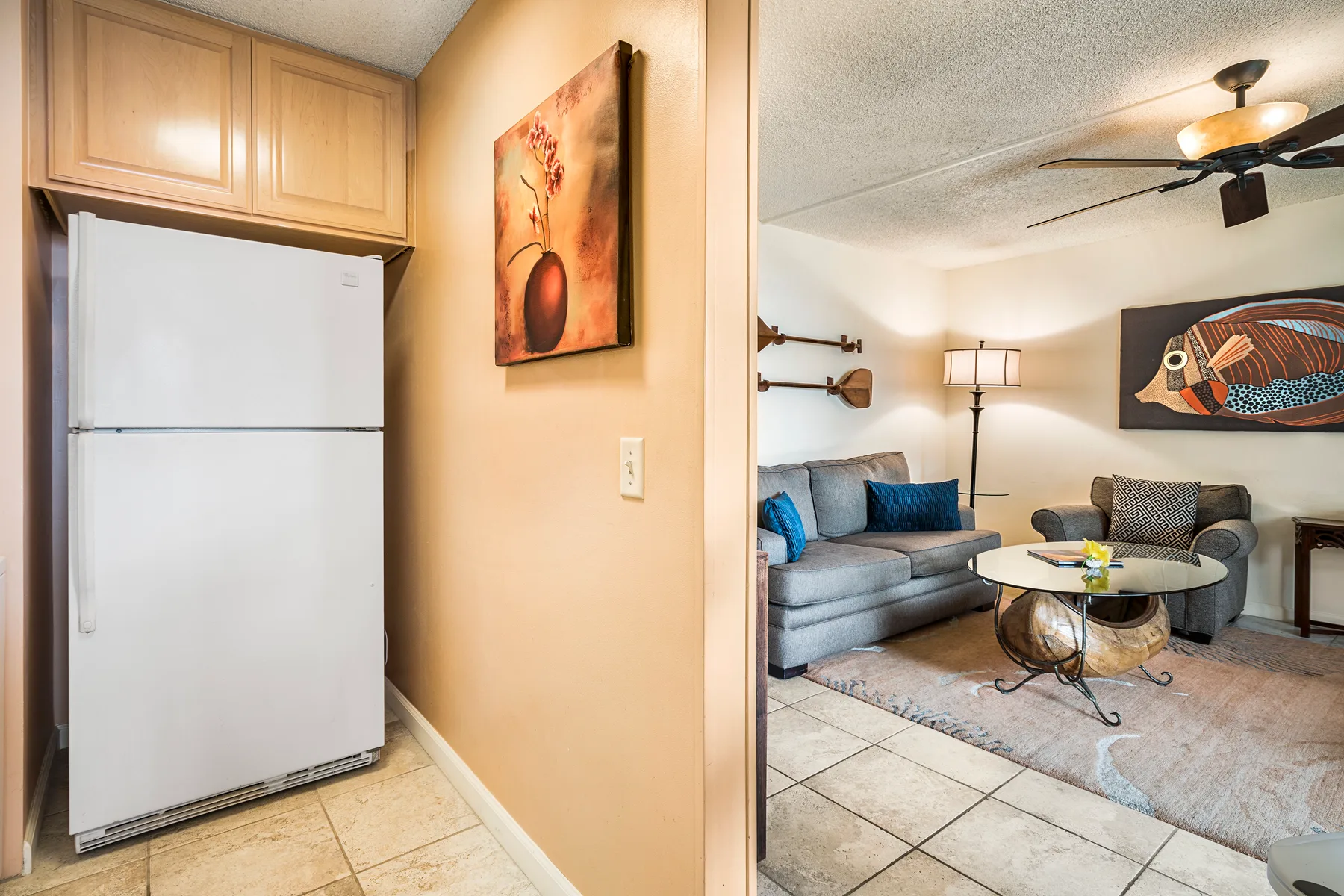 Una sala de estar con asientos, una mesa de centro y un refrigerador junto a la entrada.