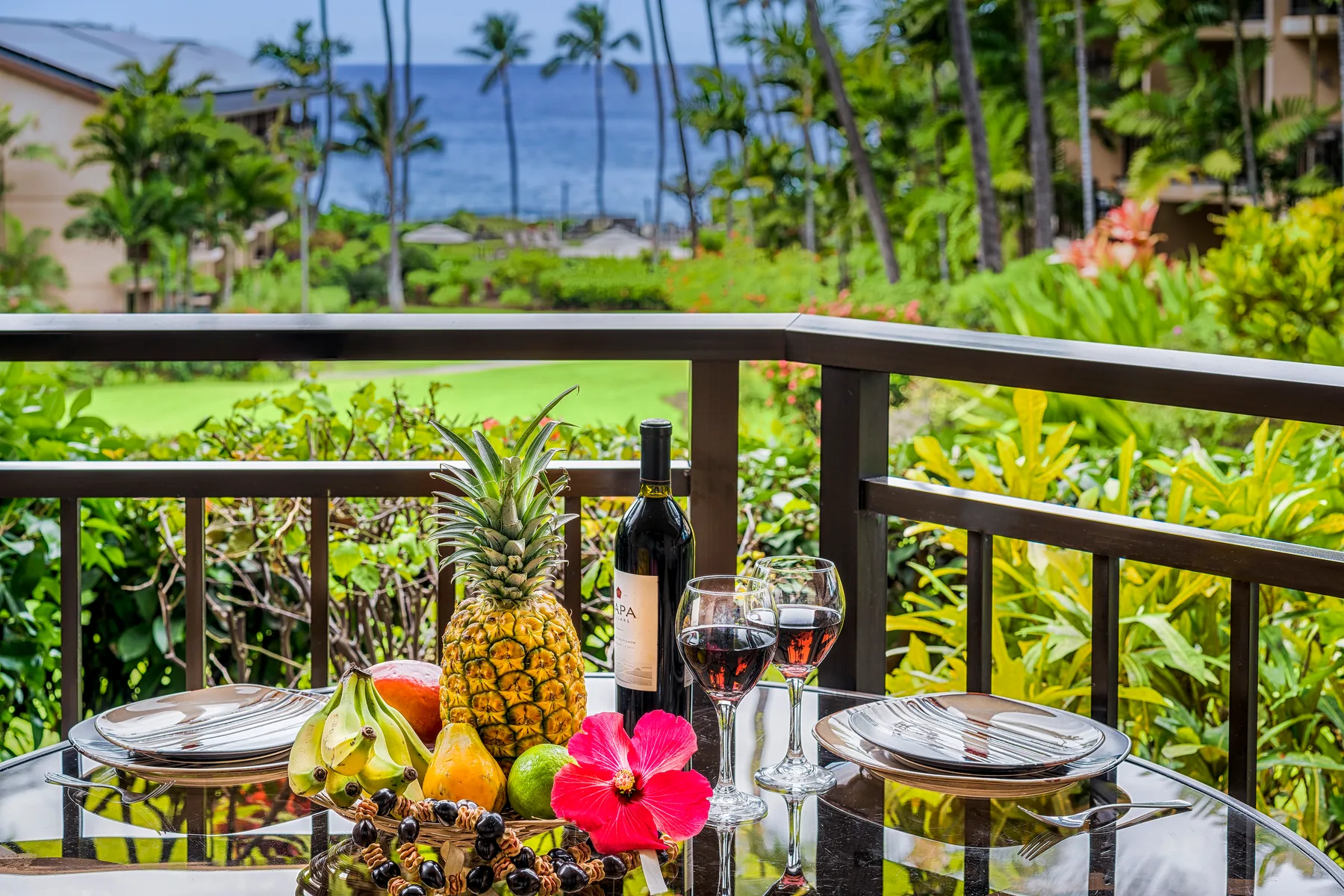 Una mesa de comedor en el balcón está puesta con platos, vino y fruta tropical.