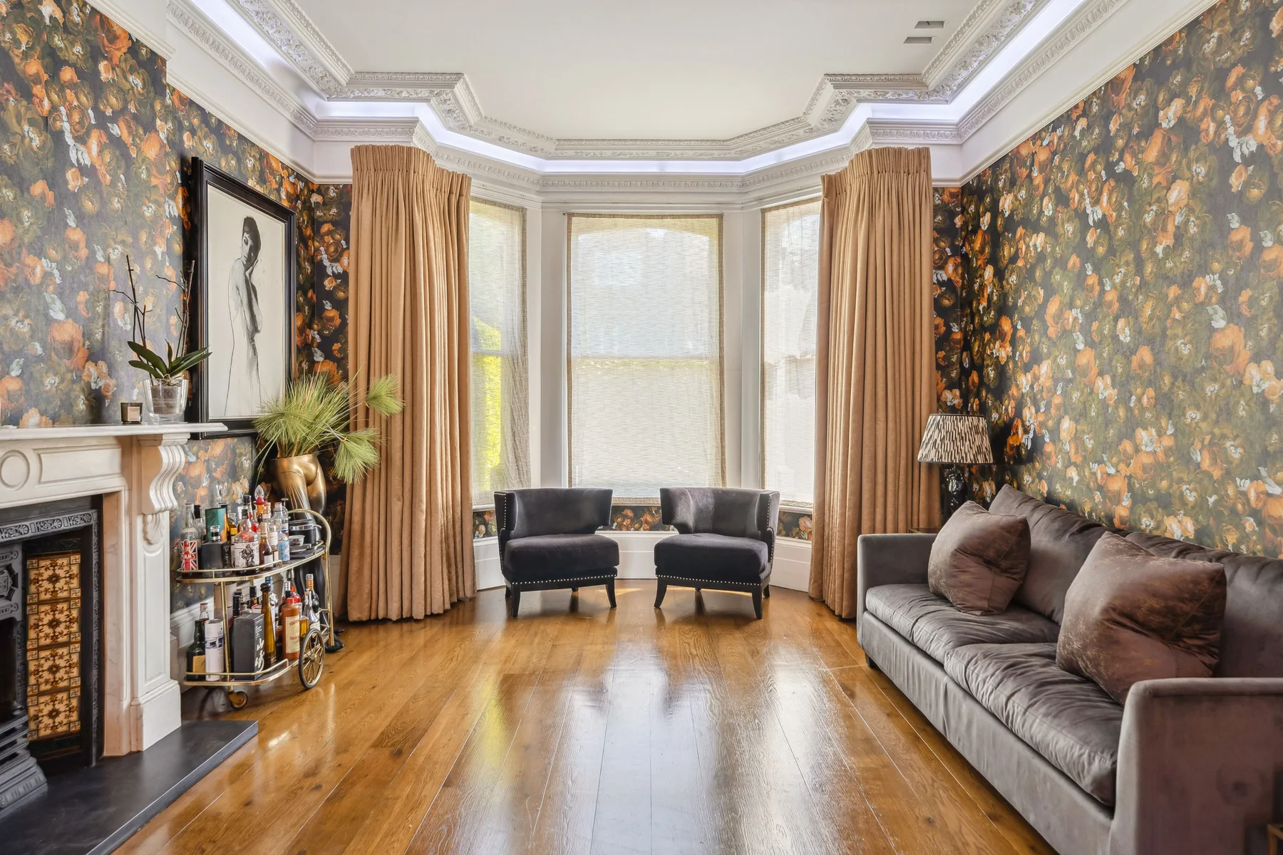 A living room with seating, large windows, and floral wallpaper.